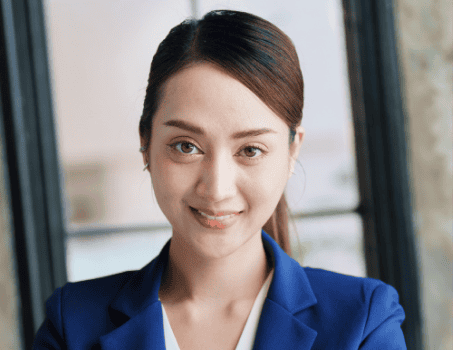 A person in a blue blazer smiles at the camera with a window in the background.