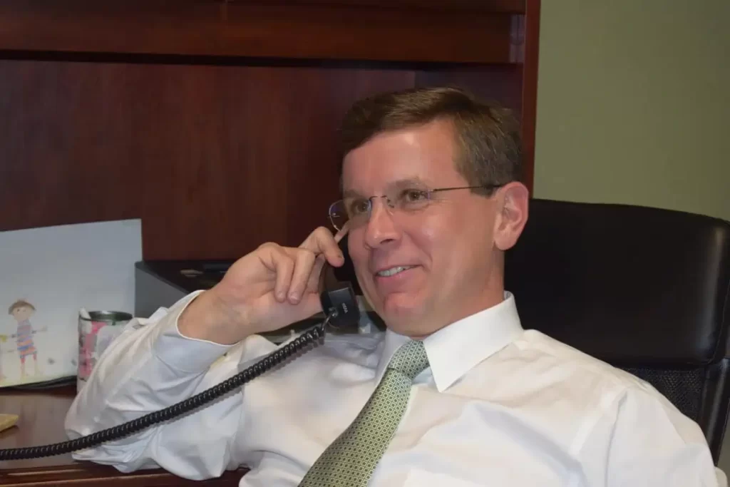 Man in a white shirt and green tie sits at a desk, smiling and talking on a corded office phone, perfect for welcoming visitors to your Homepage V1.